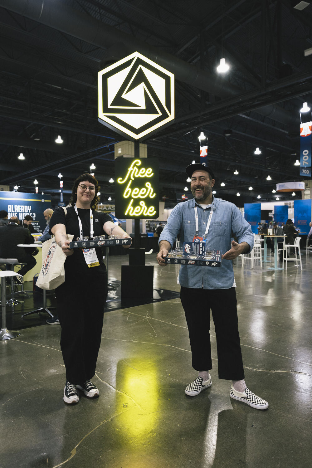 CBC attendees carrying Skunkworks tasting flights beneath the Abstrax booth sign